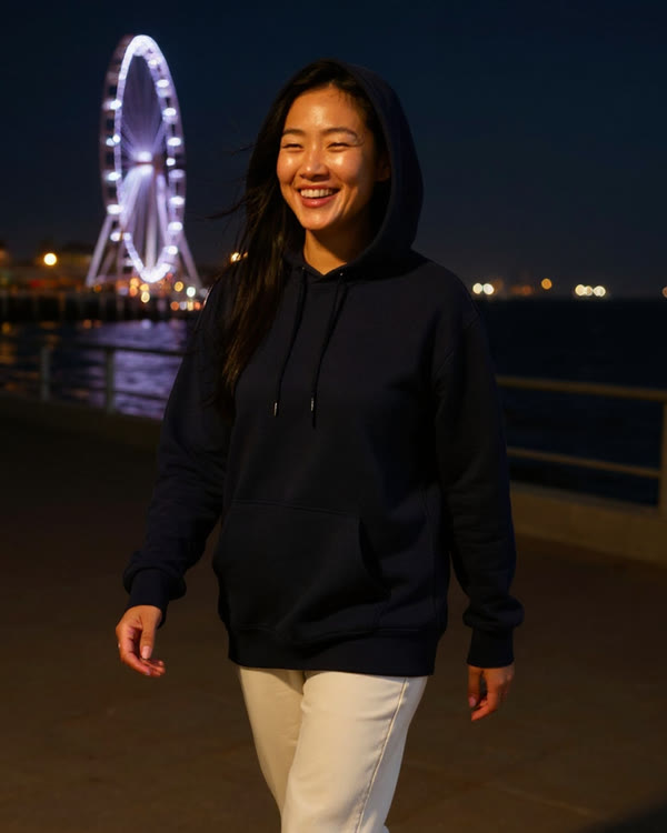 Hana, an AI character, laughing in a navy hoodie on the Santa Monica pier at night, the Ferris wheel lit behind her